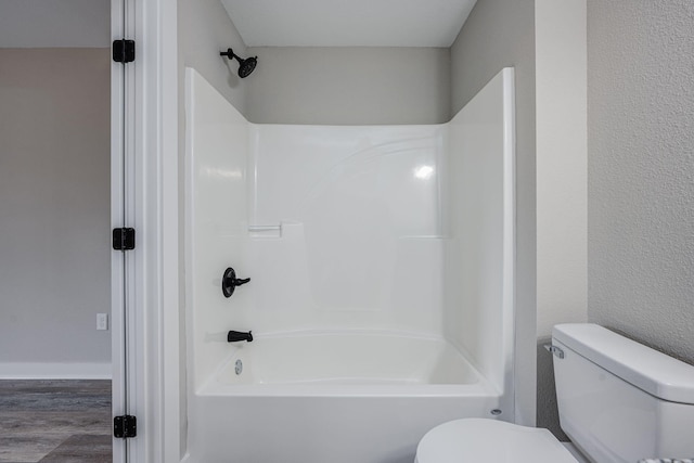 bathroom with bathing tub / shower combination, toilet, wood finished floors, and baseboards