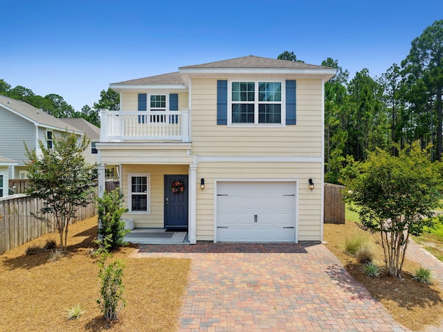 traditional-style house featuring an attached garage, decorative driveway, a balcony, and fence