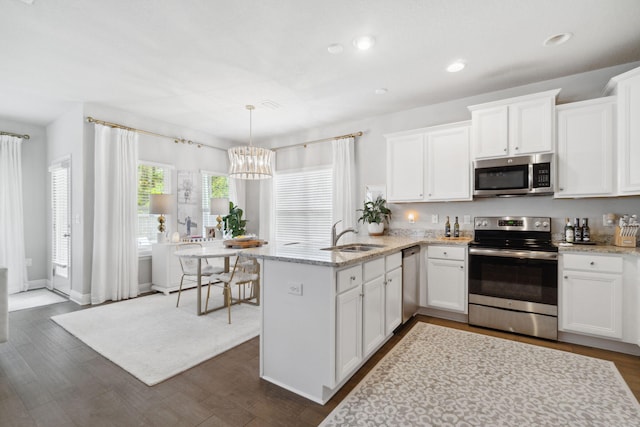 kitchen with light stone countertops, a peninsula, a sink, stainless steel appliances, and white cabinetry