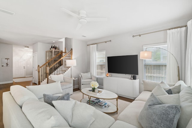 living area with visible vents, a ceiling fan, wood finished floors, and stairs