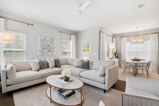 living room with visible vents, wood finished floors, and ceiling fan with notable chandelier