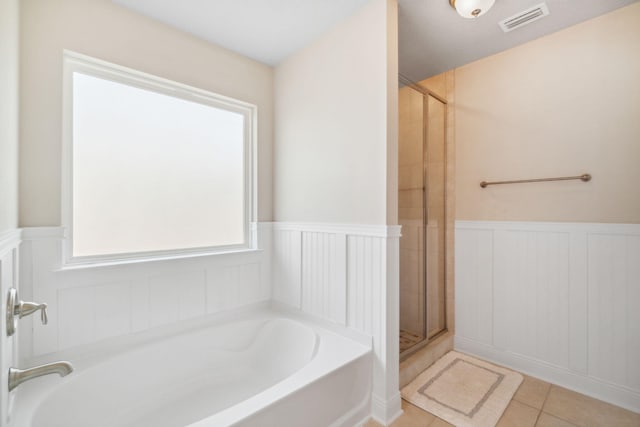 bathroom with tile patterned flooring, a bath, visible vents, and wainscoting