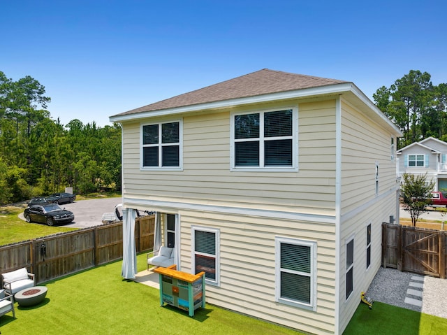 rear view of property featuring a lawn, roof with shingles, and fence