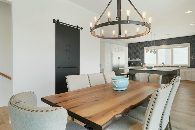 dining area with recessed lighting, a barn door, a notable chandelier, and light wood finished floors