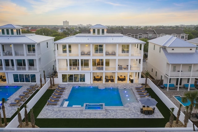 back of property at dusk featuring metal roof, a patio, and a pool with connected hot tub