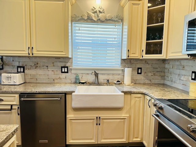 kitchen featuring tasteful backsplash, glass insert cabinets, light stone counters, appliances with stainless steel finishes, and a sink