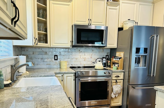 kitchen featuring a sink, glass insert cabinets, tasteful backsplash, and appliances with stainless steel finishes