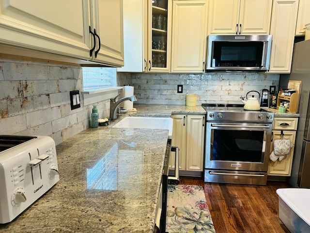 kitchen with light stone countertops, dark wood-style flooring, a sink, stainless steel appliances, and glass insert cabinets