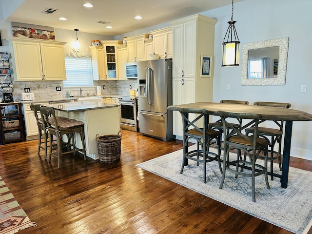 kitchen featuring a kitchen breakfast bar, backsplash, a kitchen island, dark wood finished floors, and appliances with stainless steel finishes