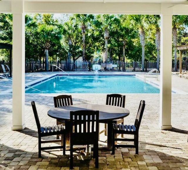 community pool featuring outdoor dining area, a patio area, and fence