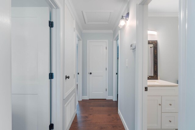 corridor with dark wood-style floors, attic access, baseboards, and ornamental molding