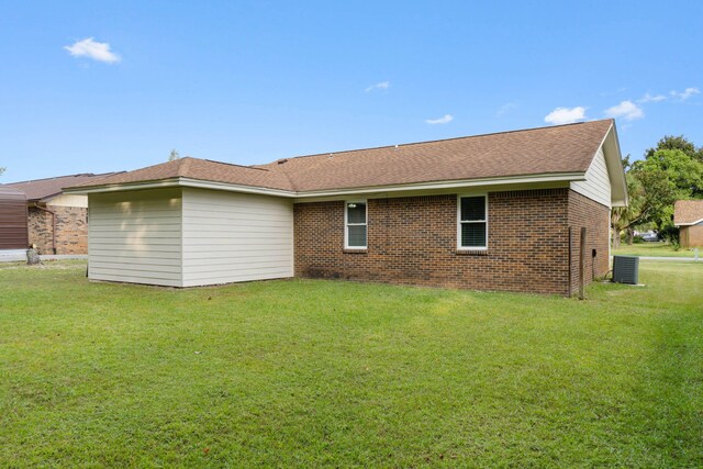 rear view of house featuring a yard, central air condition unit, brick siding, and a shingled roof