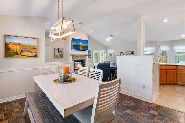 dining area with stone finish flooring, baseboards, vaulted ceiling, recessed lighting, and a glass covered fireplace