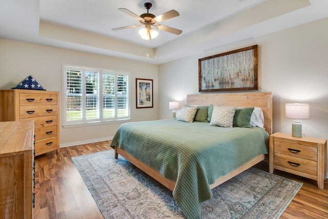 bedroom featuring baseboards, a raised ceiling, wood finished floors, and a ceiling fan