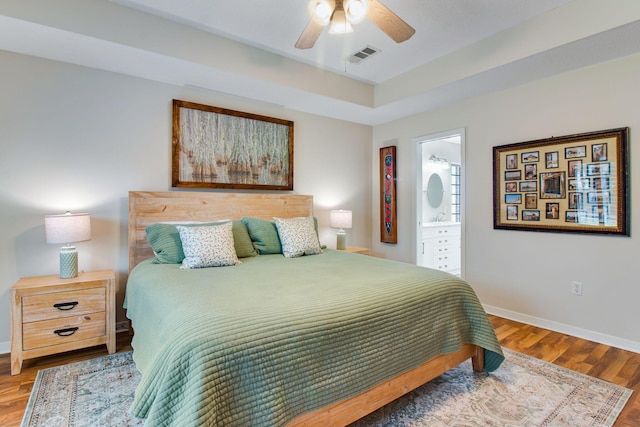 bedroom featuring visible vents, ensuite bath, baseboards, and wood finished floors