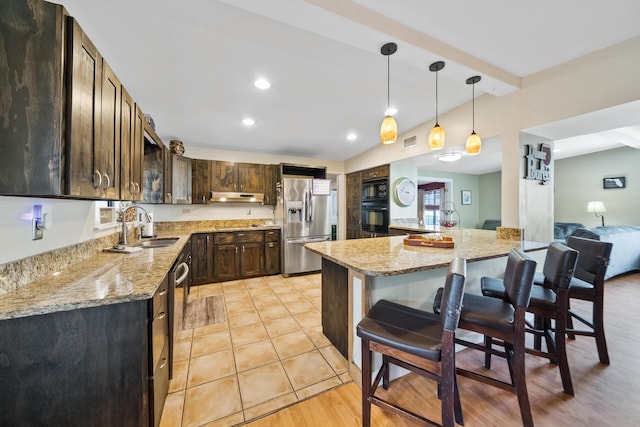 kitchen featuring a sink, stainless steel appliances, light stone counters, and dark brown cabinetry