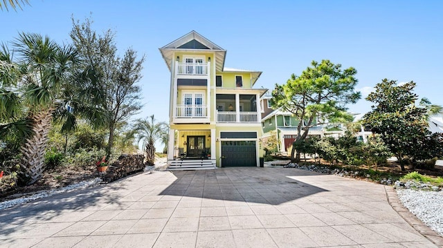 raised beach house with french doors, an attached garage, decorative driveway, and a balcony