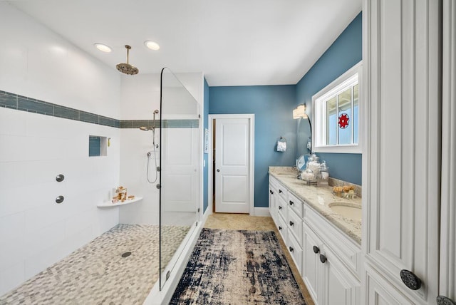 bathroom featuring a tile shower, vanity, and baseboards