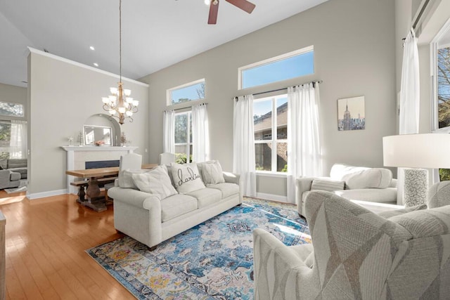 living room featuring baseboards, ceiling fan with notable chandelier, a fireplace, a towering ceiling, and hardwood / wood-style flooring