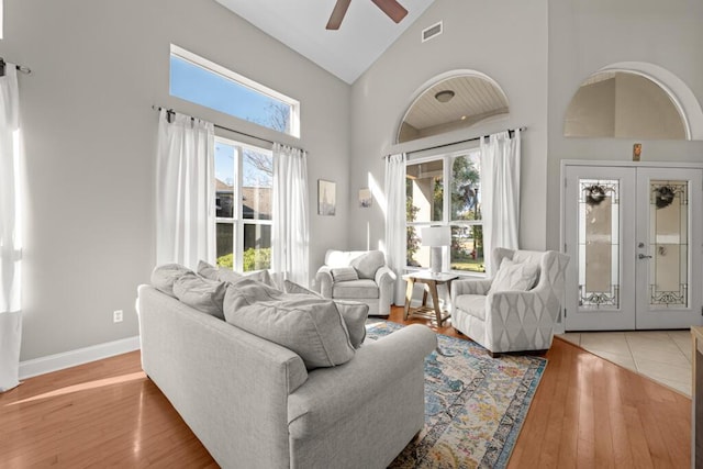 living area featuring baseboards, visible vents, high vaulted ceiling, light wood-style flooring, and french doors