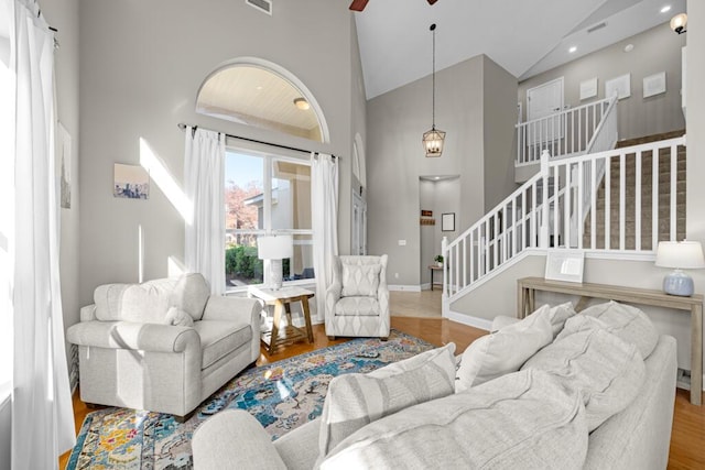 living area with a ceiling fan, high vaulted ceiling, wood finished floors, and stairs