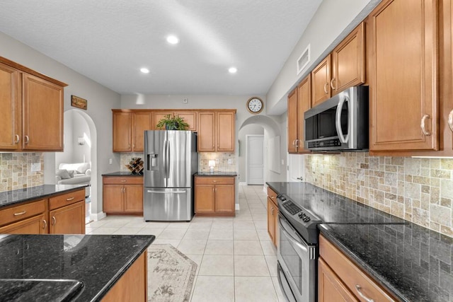 kitchen with brown cabinetry, visible vents, light tile patterned flooring, arched walkways, and appliances with stainless steel finishes