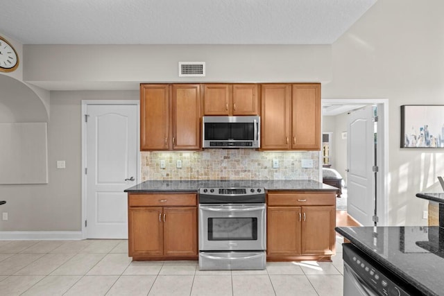 kitchen with visible vents, dark stone counters, appliances with stainless steel finishes, brown cabinetry, and light tile patterned floors