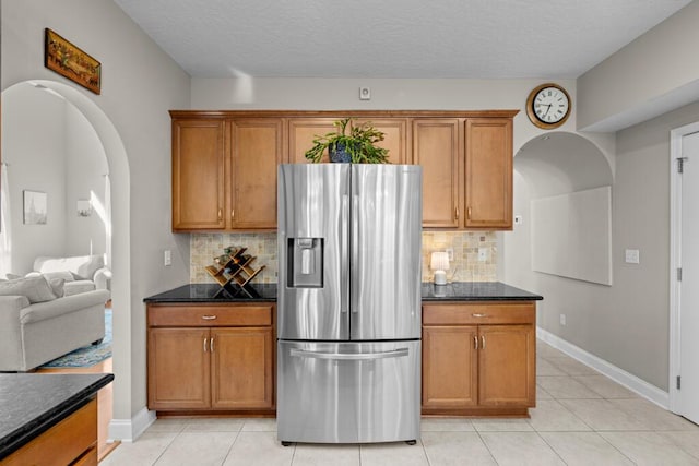 kitchen with decorative backsplash, brown cabinetry, stainless steel fridge with ice dispenser, and arched walkways