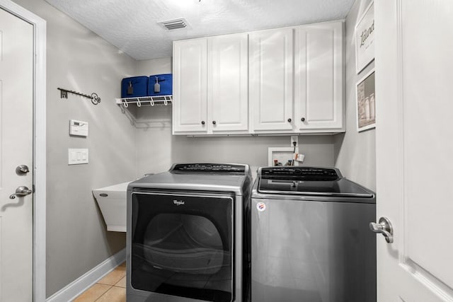 washroom featuring light tile patterned floors, visible vents, washing machine and clothes dryer, cabinet space, and a textured ceiling