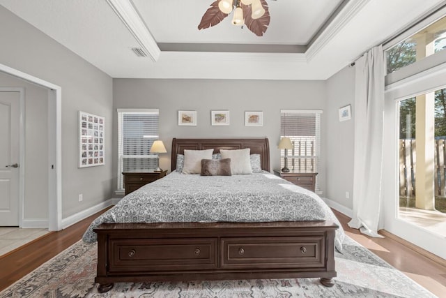 bedroom with wood finished floors, visible vents, baseboards, a tray ceiling, and access to outside