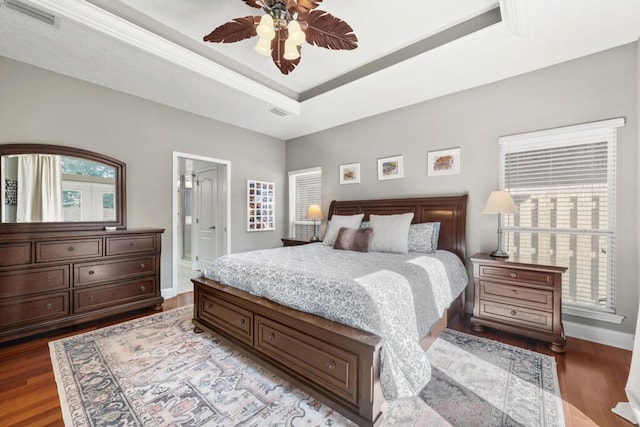 bedroom featuring wood finished floors, visible vents, baseboards, a tray ceiling, and ornamental molding