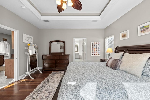 bedroom featuring ensuite bath, a raised ceiling, baseboards, and wood finished floors