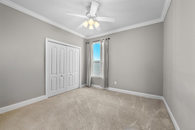 unfurnished bedroom featuring a ceiling fan, a closet, carpet floors, crown molding, and baseboards