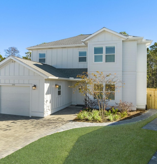 view of front facade featuring board and batten siding, roof with shingles, a front yard, decorative driveway, and an attached garage