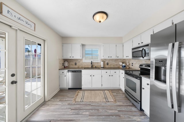 kitchen featuring decorative backsplash, white cabinets, light wood-style floors, and stainless steel appliances