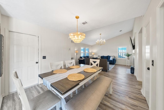 dining room featuring light wood finished floors, visible vents, baseboards, vaulted ceiling, and a notable chandelier