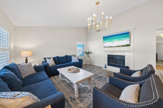 living area featuring a tiled fireplace, a notable chandelier, wood finished floors, and baseboards