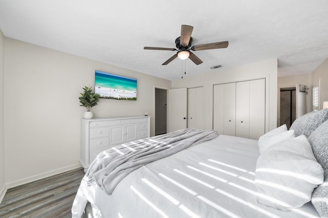 bedroom with wood finished floors, visible vents, baseboards, ceiling fan, and multiple closets