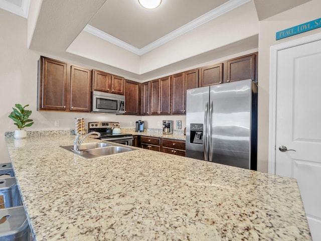 kitchen featuring a peninsula, a tray ceiling, ornamental molding, stainless steel appliances, and a kitchen bar