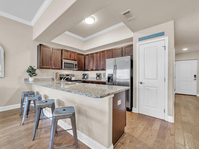 kitchen with visible vents, a sink, a peninsula, appliances with stainless steel finishes, and a breakfast bar area