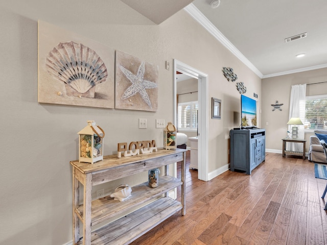 hallway with visible vents, plenty of natural light, crown molding, and wood finished floors