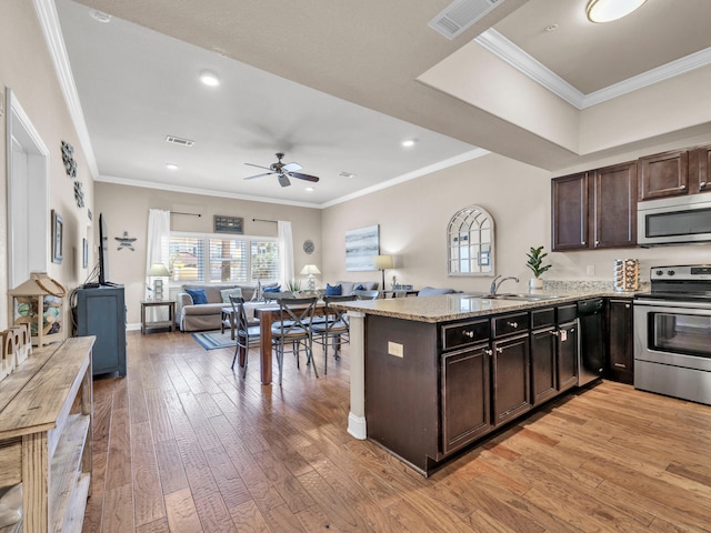 kitchen featuring open floor plan, dark brown cabinets, stainless steel appliances, and a sink