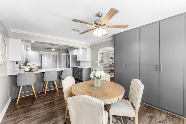 dining space with a ceiling fan, visible vents, dark wood finished floors, arched walkways, and ornamental molding