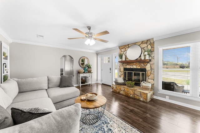 living area featuring visible vents, arched walkways, a stone fireplace, dark wood-type flooring, and crown molding