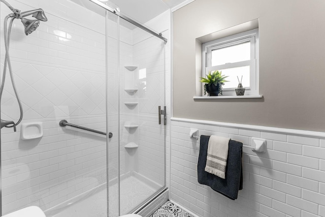 bathroom featuring wainscoting, a stall shower, and tile walls