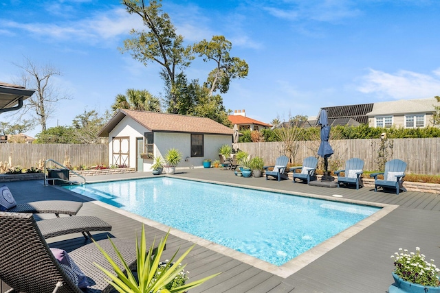 view of swimming pool featuring an outbuilding, a fenced in pool, a wooden deck, a fenced backyard, and a patio area