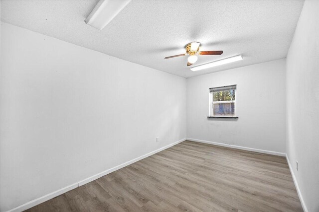 empty room with ceiling fan, a textured ceiling, baseboards, and wood finished floors