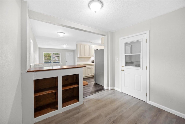 kitchen with wood finished floors, baseboards, freestanding refrigerator, a textured ceiling, and white cabinetry