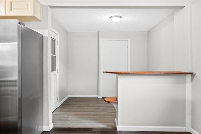 kitchen with a textured ceiling, freestanding refrigerator, baseboards, and wood finished floors