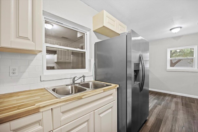 kitchen featuring tasteful backsplash, a sink, baseboards, stainless steel refrigerator with ice dispenser, and dark wood-style flooring